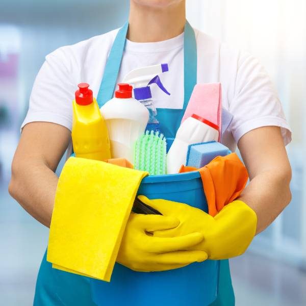 Professional house cleaner holding a bucket full of cleaning products, bottles, and other tools.